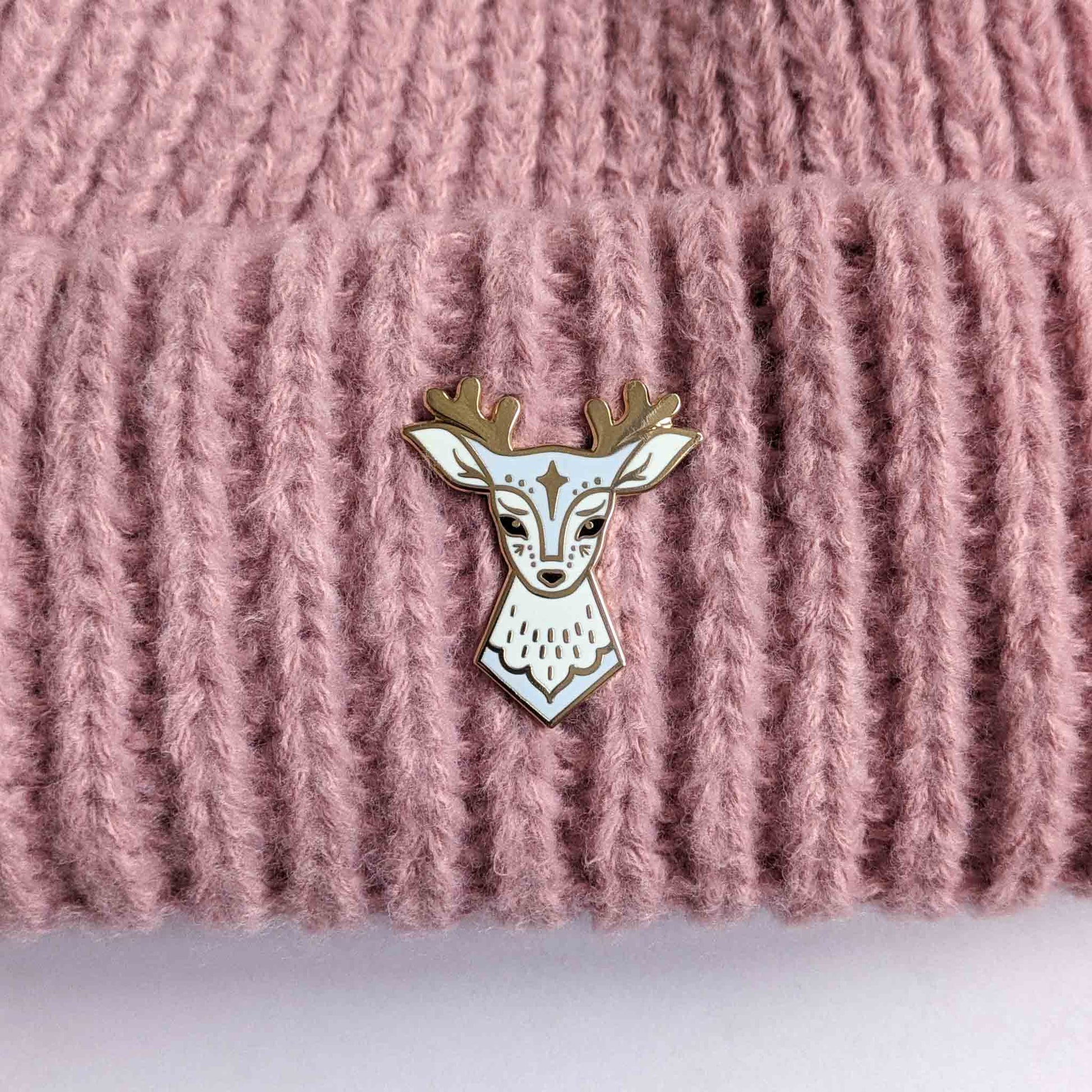 Blue deer enamel pin with star design by Looksee Illustration, on a knitted hat