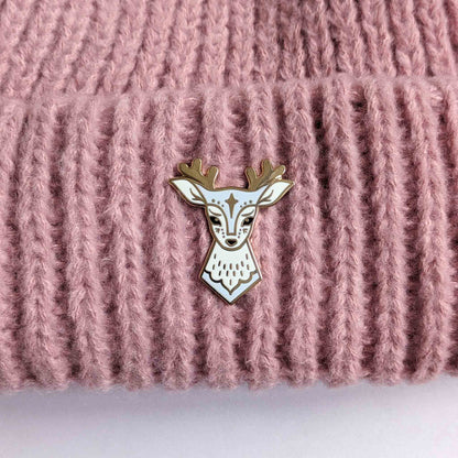 Blue deer enamel pin with star design by Looksee Illustration, on a knitted hat